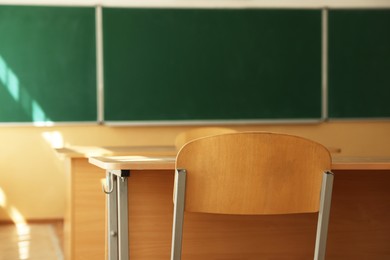Photo of Desks with chairs and green chalkboard in classroom, selective focus