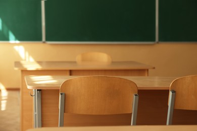 Photo of Desks with chairs and green chalkboard in classroom, selective focus