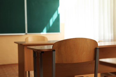 Photo of Desks with chairs and green chalkboard in classroom, selective focus