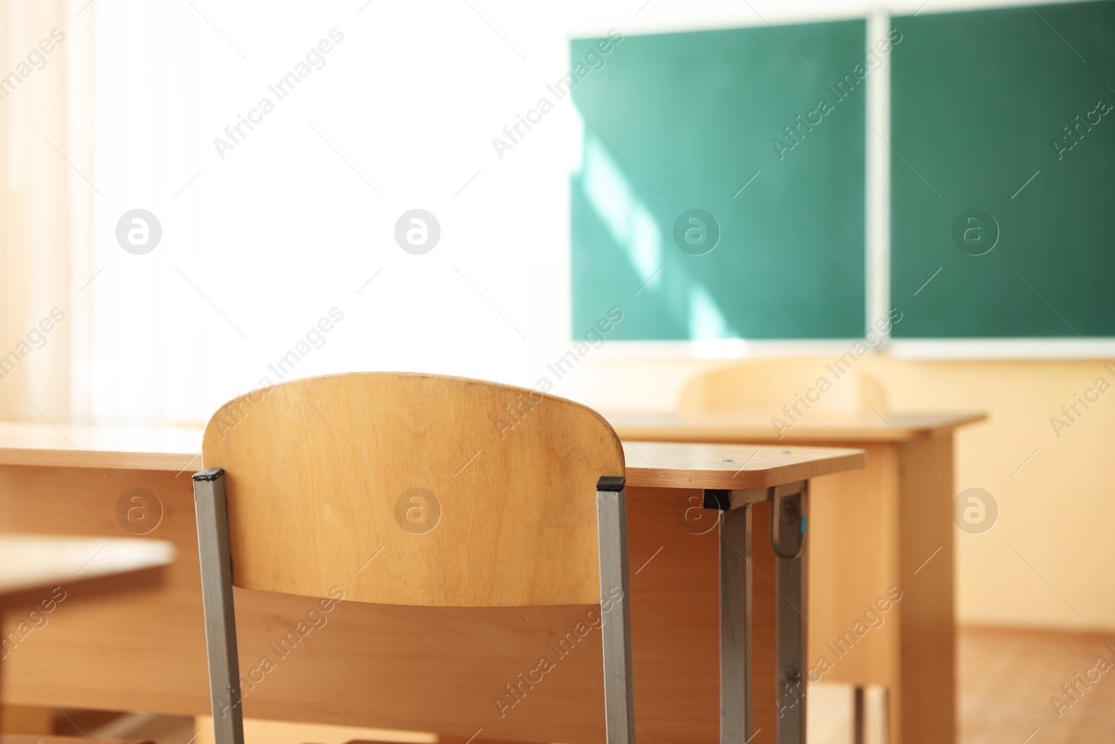 Photo of Desks with chairs and green chalkboard in classroom, selective focus