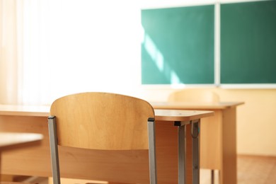 Photo of Desks with chairs and green chalkboard in classroom, selective focus
