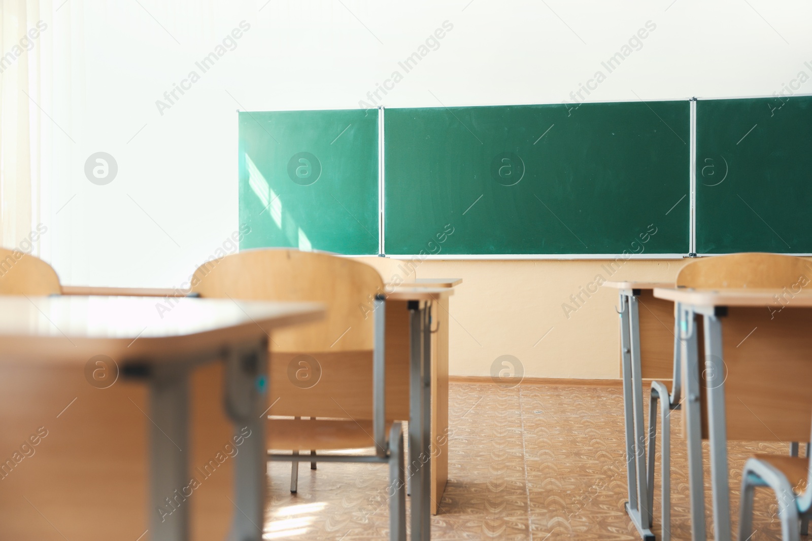 Photo of Desks with chairs and green chalkboard in classroom