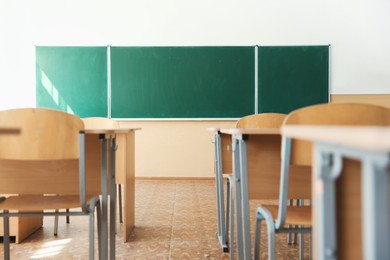 Photo of Desks with chairs and green chalkboard in classroom