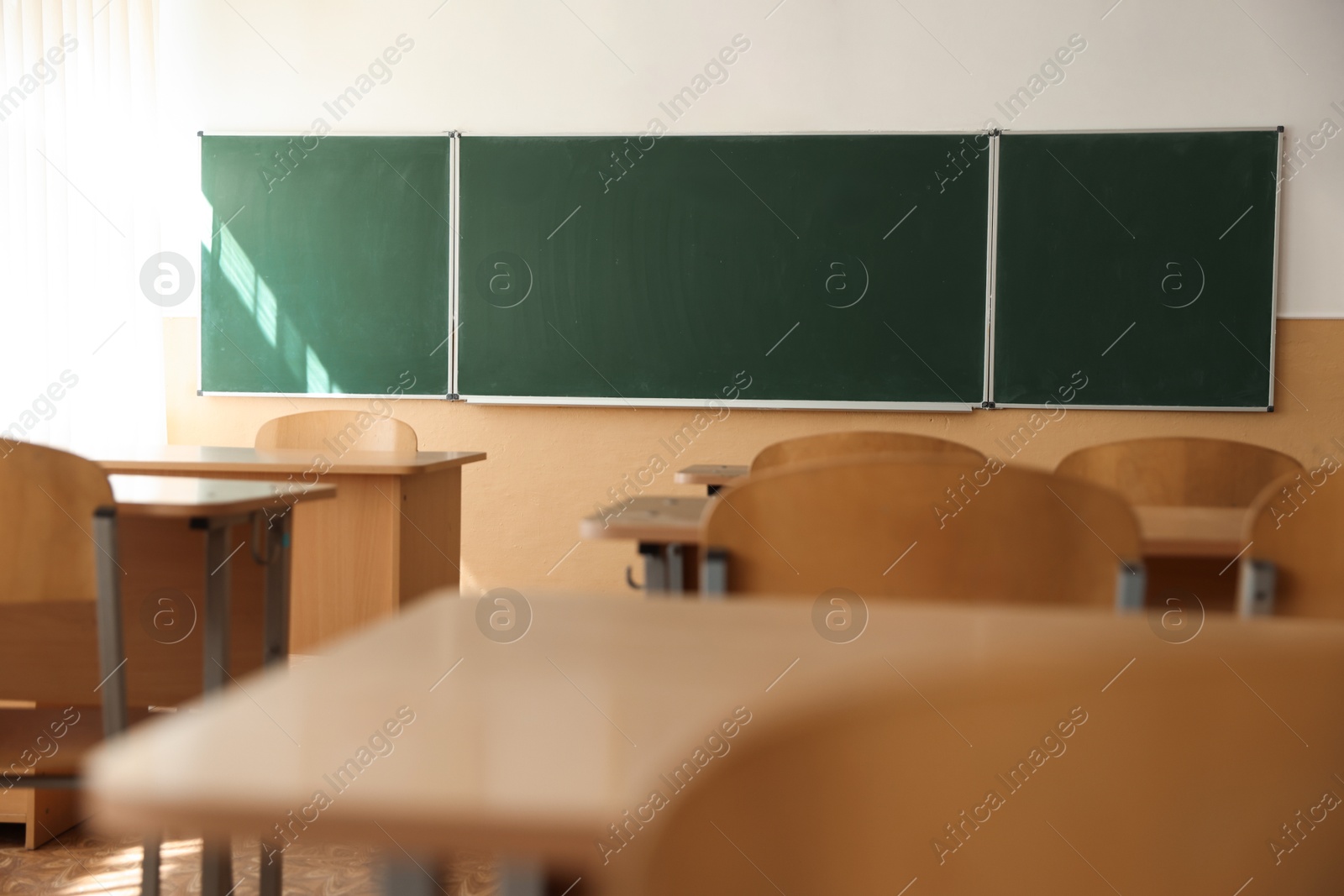Photo of Desks with chairs and green chalkboard in classroom