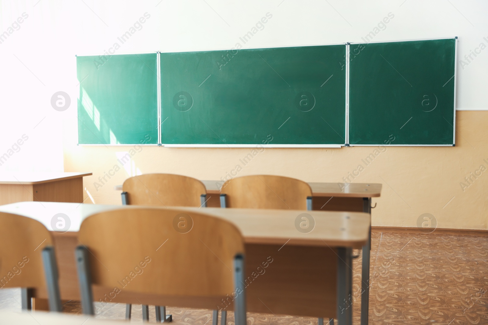 Photo of Desks with chairs and green chalkboard in classroom