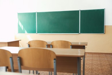 Photo of Desks with chairs and green chalkboard in classroom