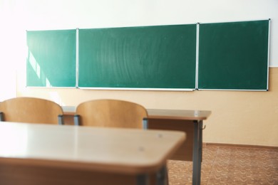 Photo of Desks with chairs and green chalkboard in classroom