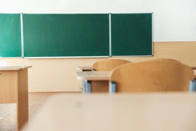 Photo of Desks with chairs and green chalkboard in classroom