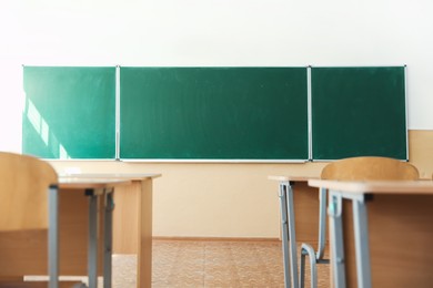 Photo of Desks with chairs and green chalkboard in classroom