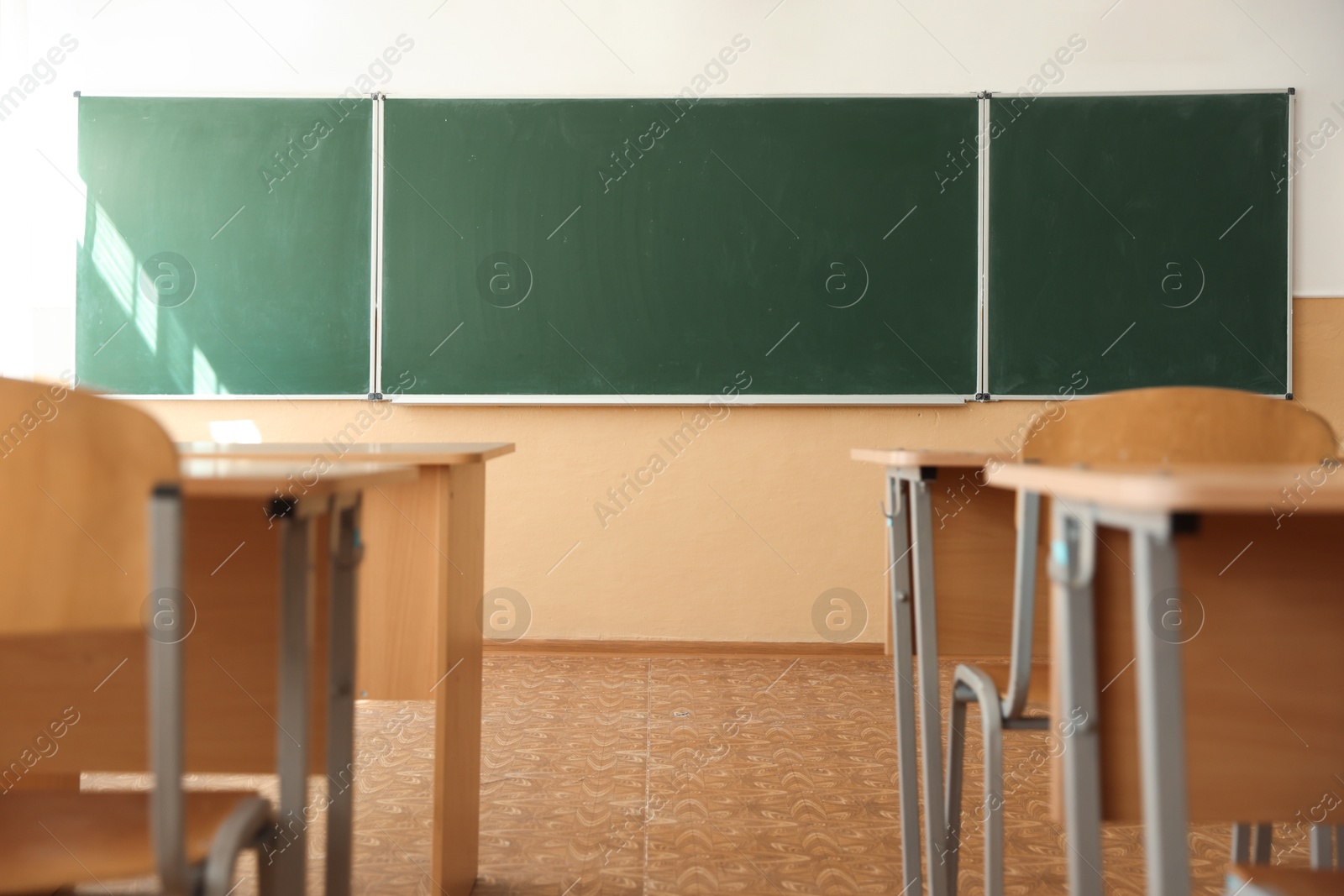 Photo of Desks with chairs and green chalkboard in classroom