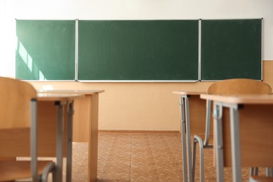 Photo of Desks with chairs and green chalkboard in classroom