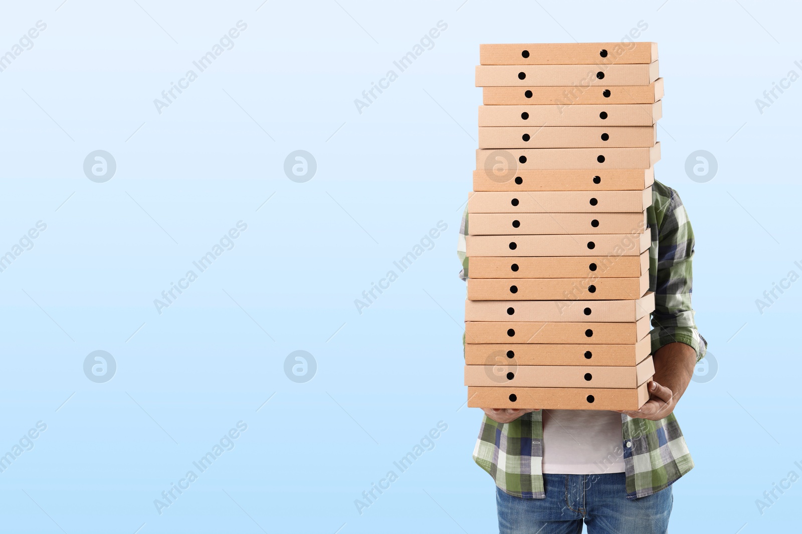 Man holding many pizza boxes against light blue gradient background. Space for text Image of Man holding many pizza boxes against light blue gradient background. Space for text