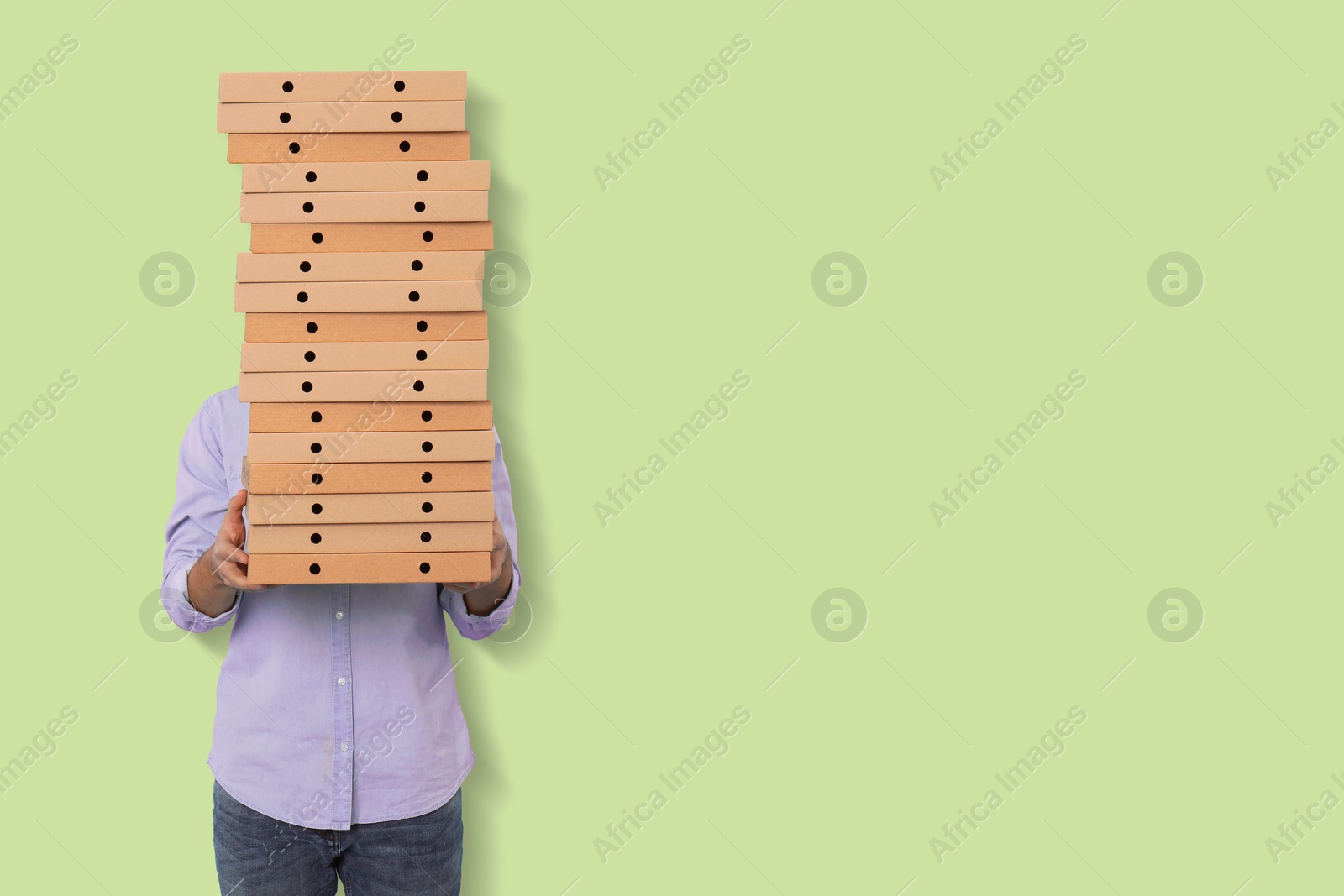 Image of Man holding many pizza boxes against light green background. Space for text