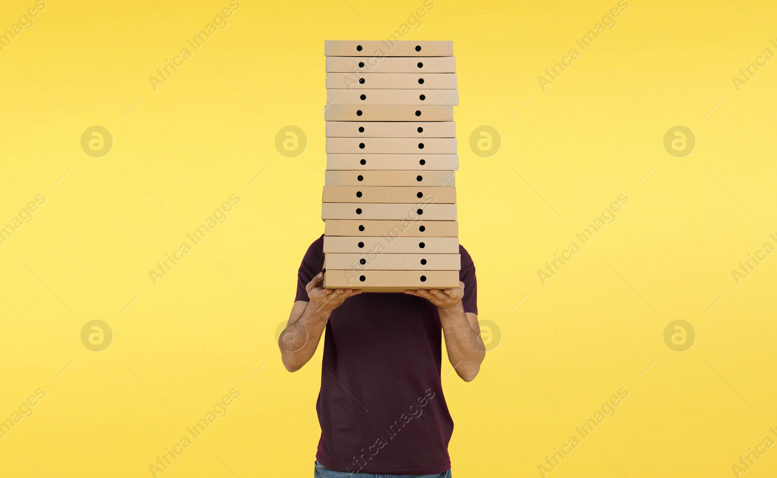 Man holding many pizza boxes against yellow background Image of Man holding many pizza boxes against yellow background