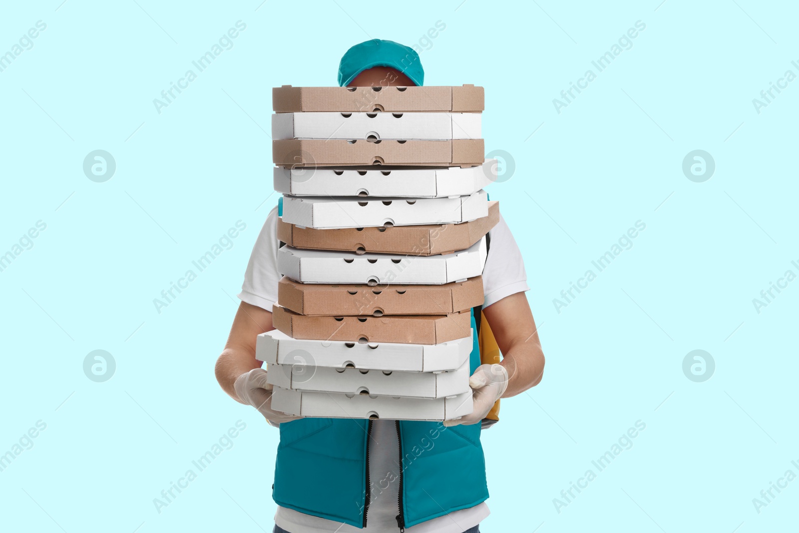 Deliveryman holding many pizza boxes against light blue background Image of Deliveryman holding many pizza boxes against light blue background