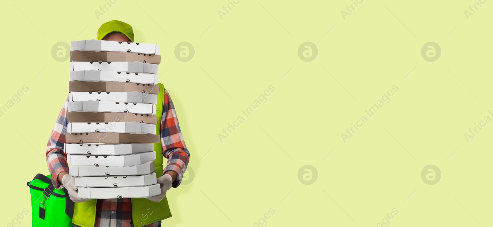 Deliveryman holding many pizza boxes against light yellowish green background. Banner design with space for text Image of Deliveryman holding many pizza boxes against light yellowish green background. Banner design with space for text