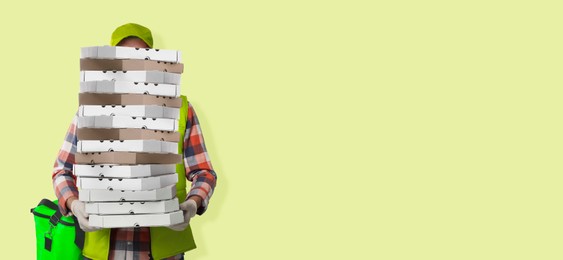 Image of Deliveryman holding many pizza boxes against light yellowish green background. Banner design with space for text