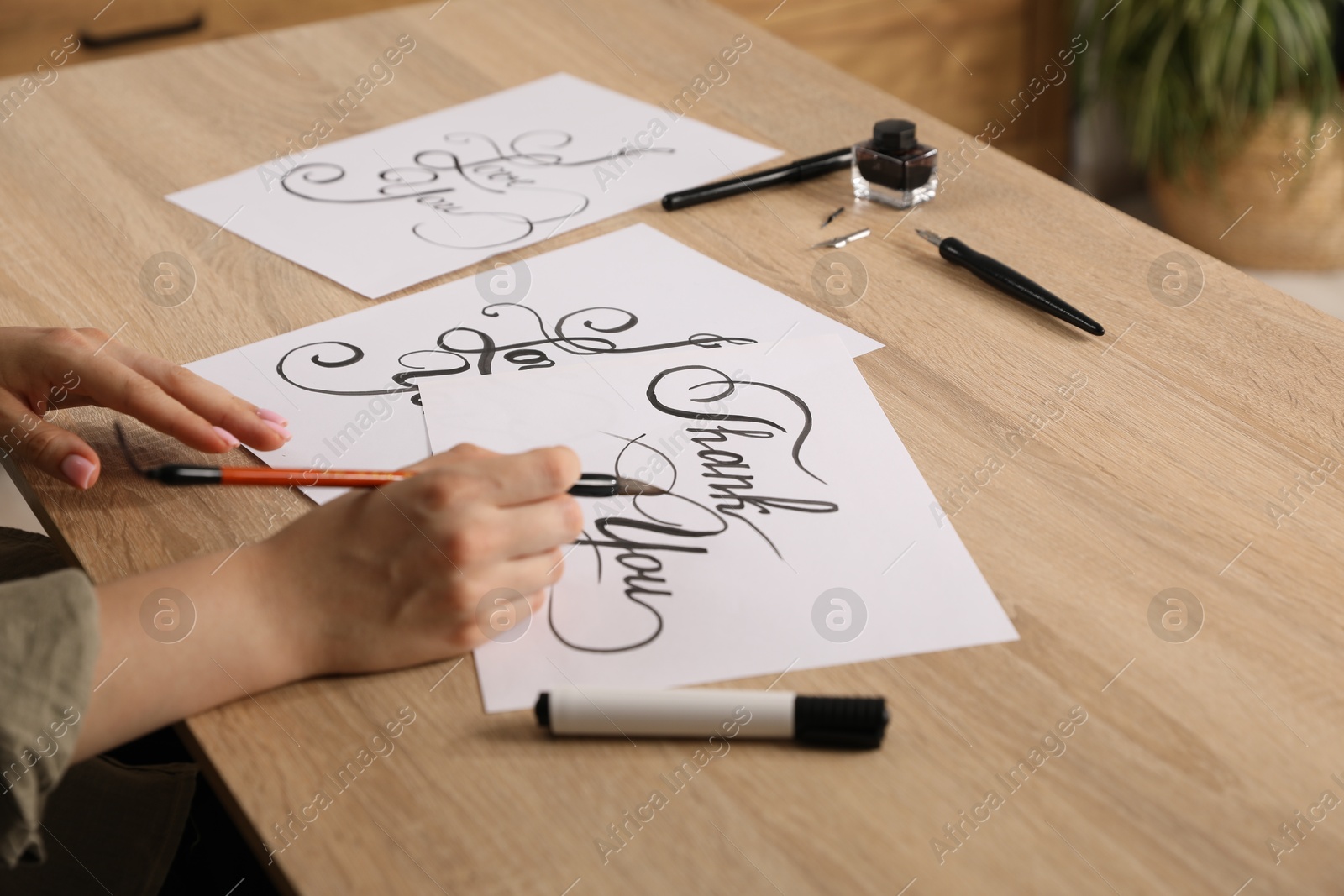 Calligraphy. Woman with brush writing words Thank You on sheet of paper at wooden table, closeup Photo of Calligraphy. Woman with brush writing words Thank You on sheet of paper at wooden table, closeup
