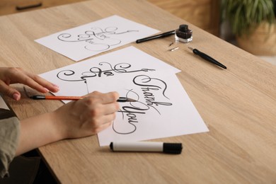 Photo of Calligraphy. Woman with brush writing words Thank You on sheet of paper at wooden table, closeup