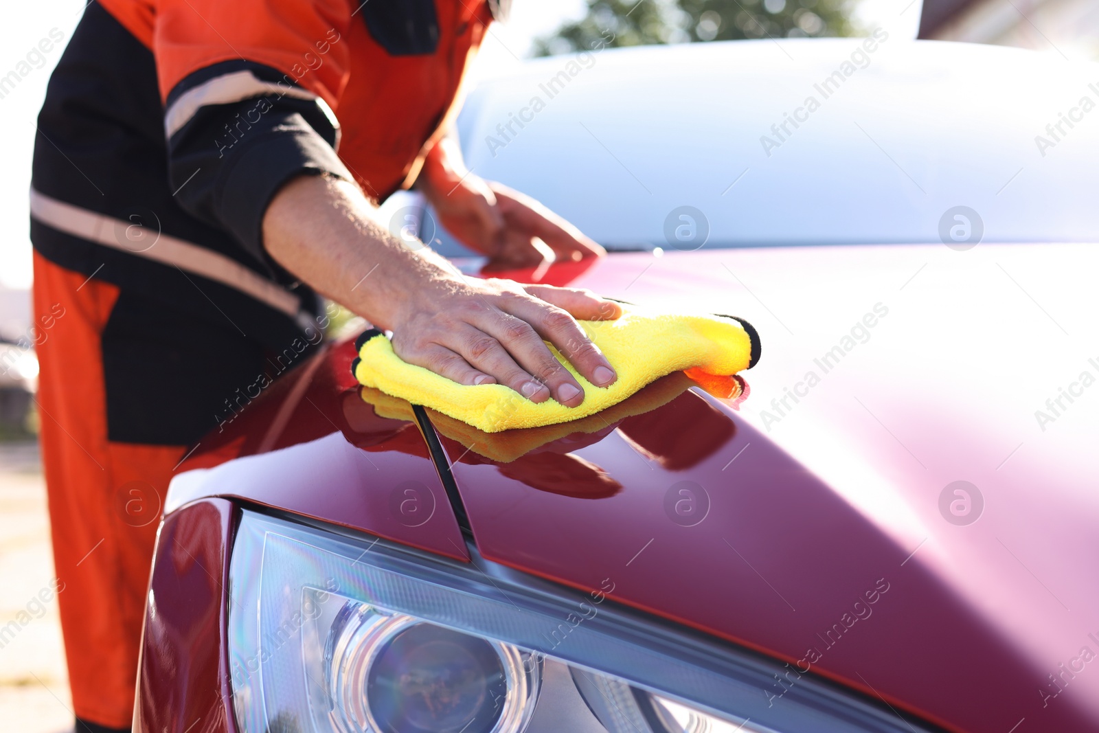 Photo of Man wiping car hood with yellow microfiber rag outdoors, closeup