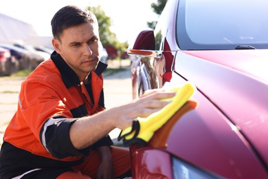 Photo of Man wiping car hood with yellow microfiber rag outdoors