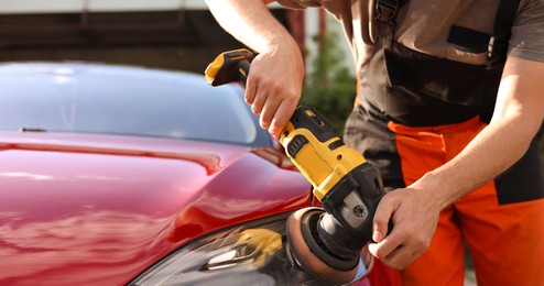Photo of Man polishing car headlight with orbital polisher outdoors, closeup