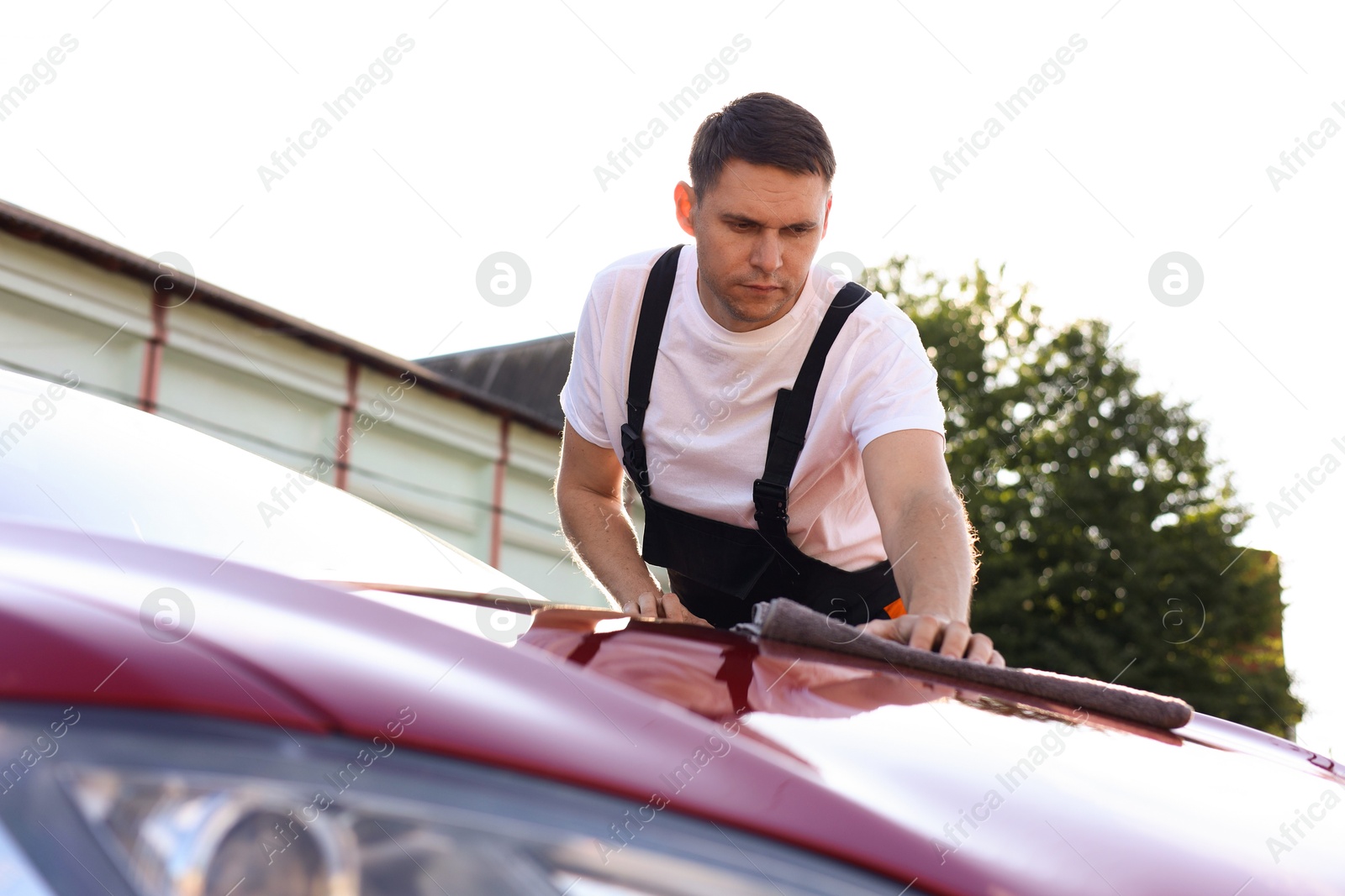 Photo of Man wiping car hood with grey microfiber rag outdoors
