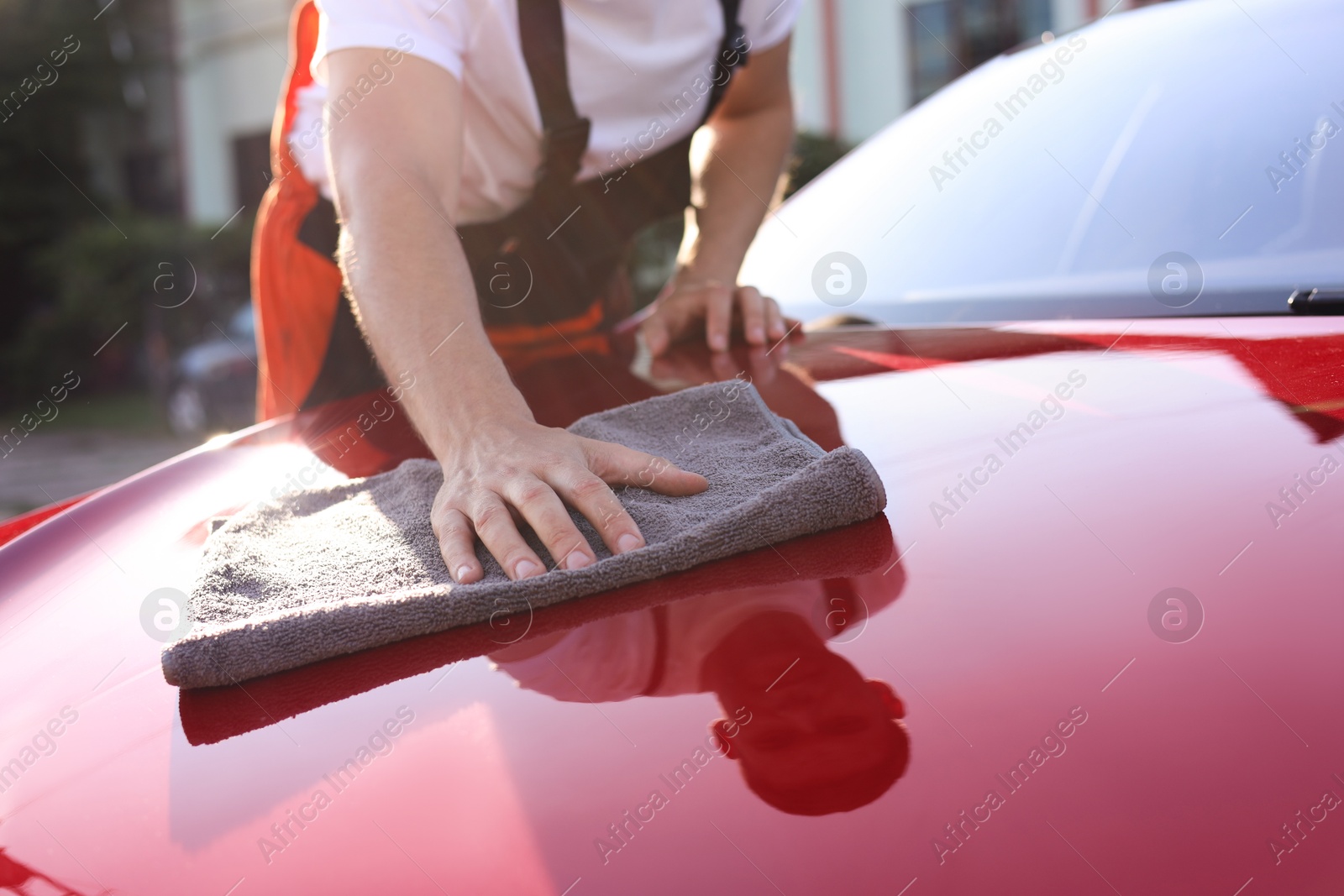 Photo of Man wiping car hood with grey microfiber rag outdoors, closeup