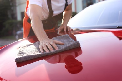 Photo of Man wiping car hood with grey microfiber rag outdoors, closeup