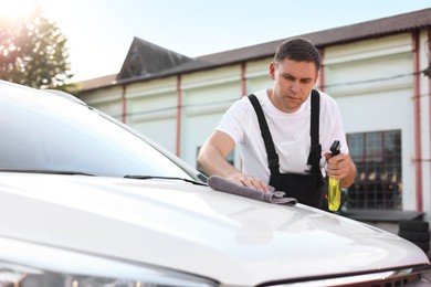 Photo of Man wiping car with grey microfiber rag outdoors
