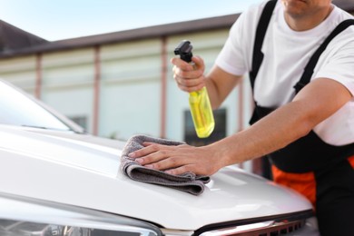 Photo of Man wiping car hood with grey microfiber rag outdoors, closeup