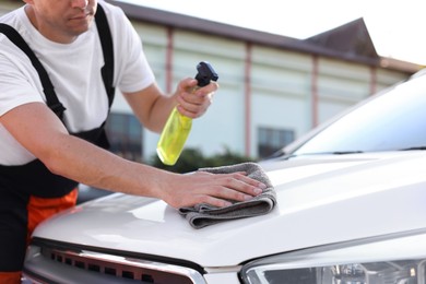 Photo of Man wiping car hood with grey microfiber rag outdoors, closeup