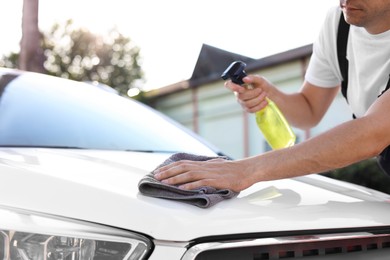 Photo of Man wiping car hood with grey microfiber rag outdoors, closeup