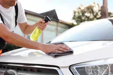 Photo of Man wiping car hood with grey microfiber rag outdoors, closeup