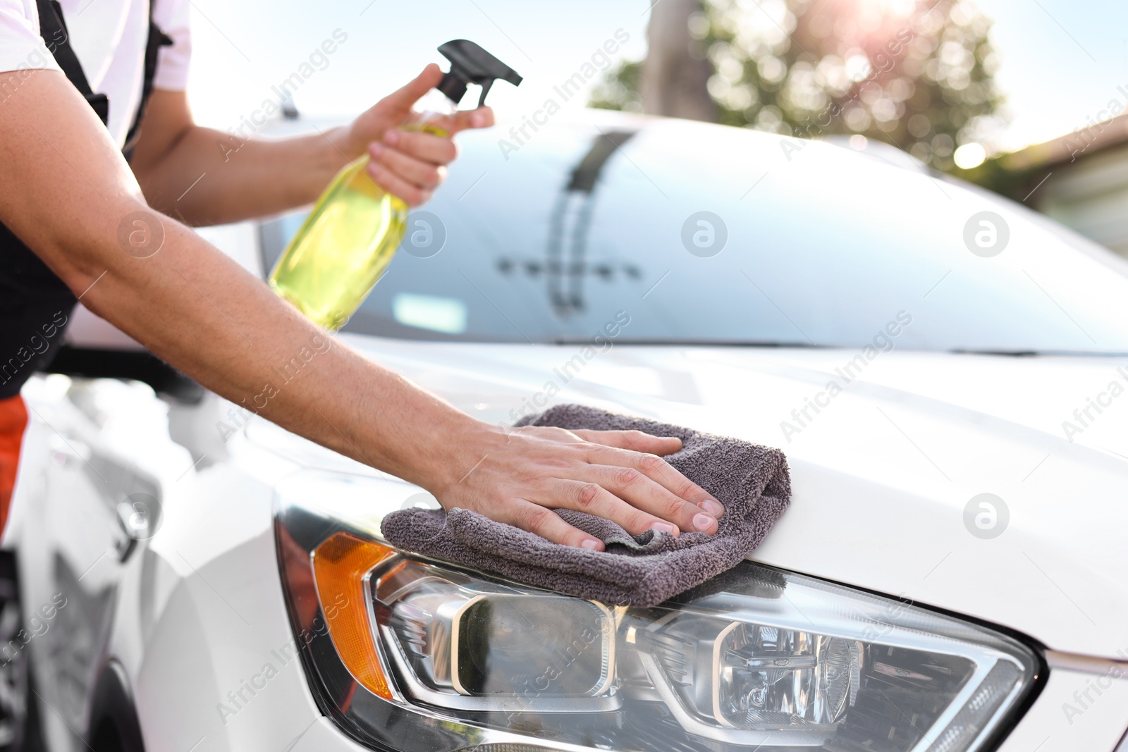 Photo of Man wiping car headlight with grey microfiber rag outdoors, closeup