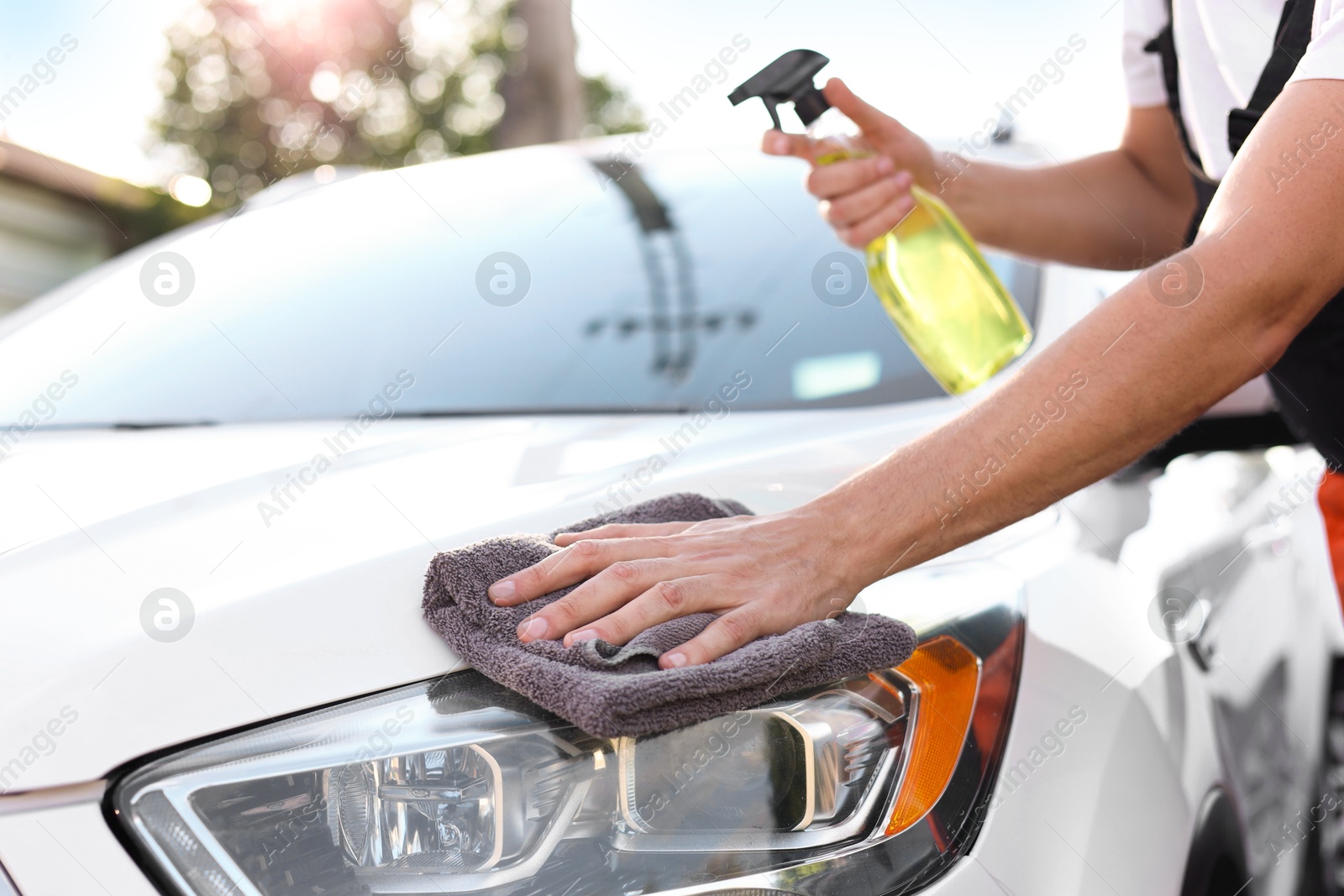 Photo of Man wiping car headlight with grey microfiber rag outdoors, closeup