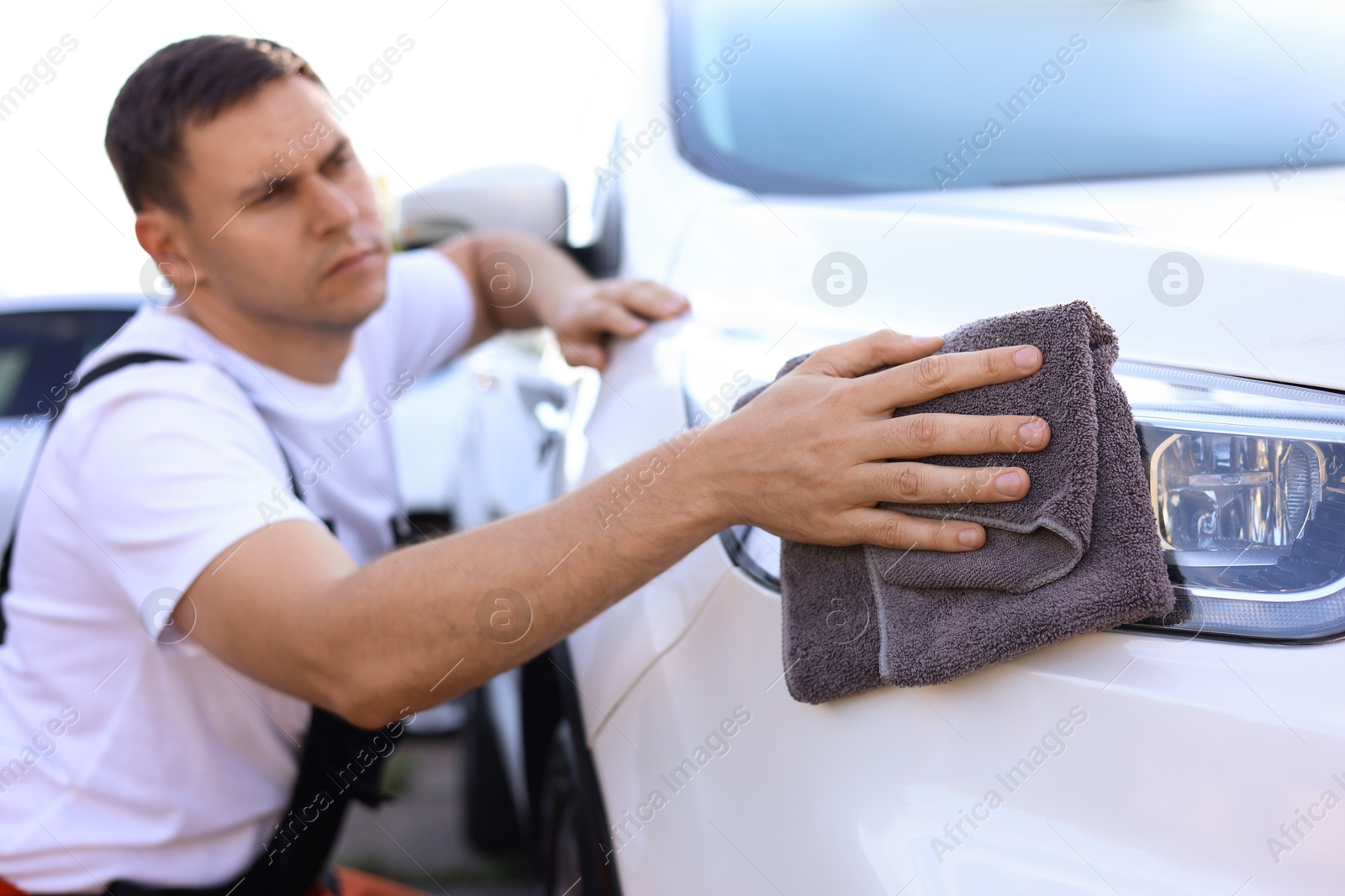 Man wiping car headlight with grey microfiber rag outdoors, closeup Photo of Man wiping car headlight with grey microfiber rag outdoors, closeup