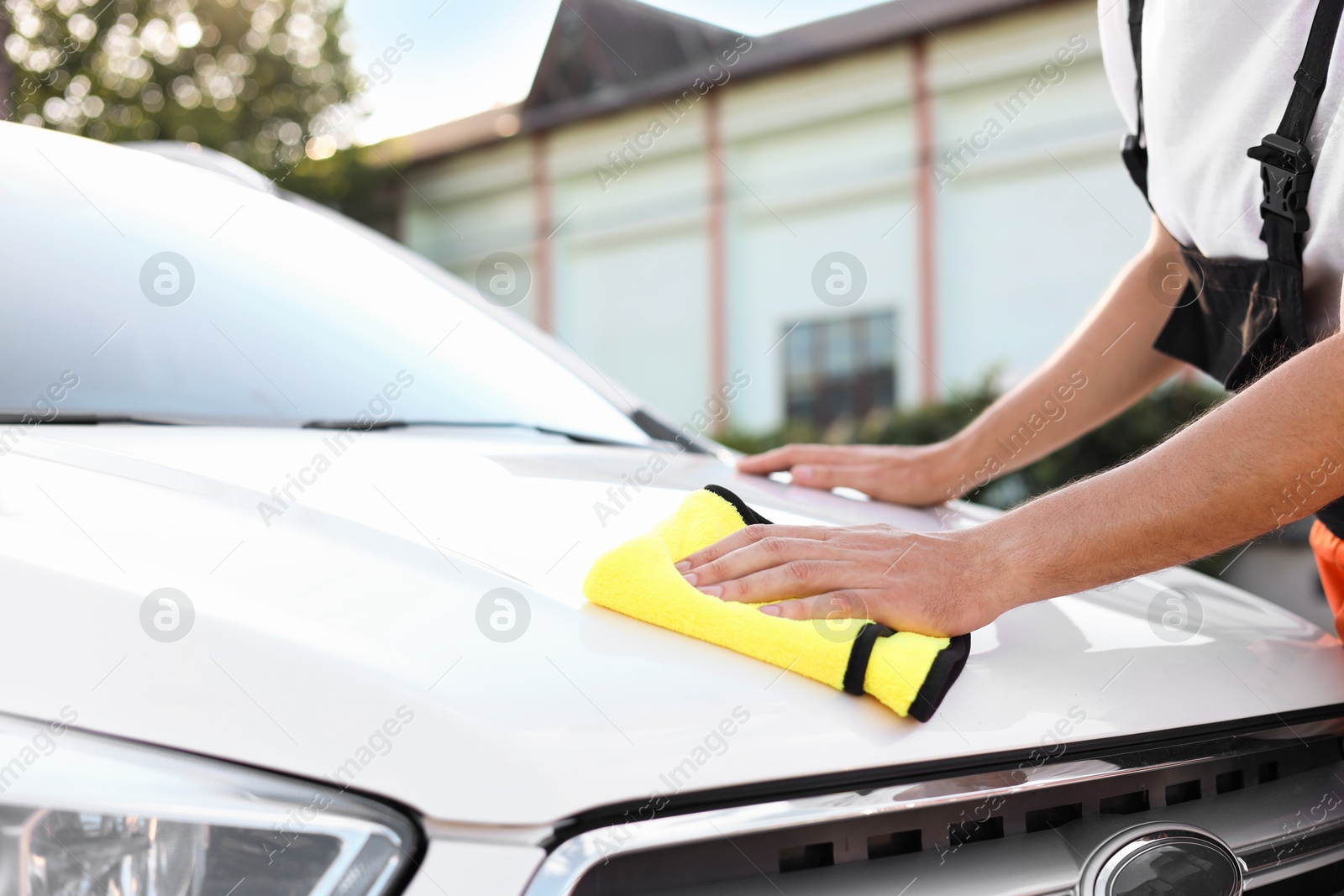 Photo of Man wiping car hood with yellow microfiber rag outdoors, closeup