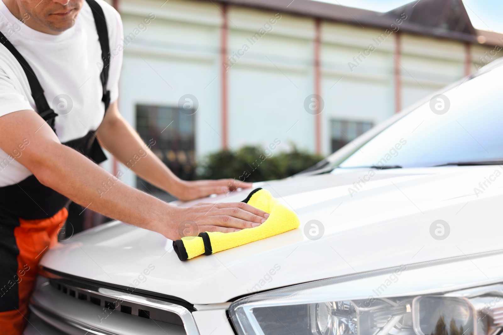 Photo of Man wiping car hood with yellow microfiber rag outdoors, closeup