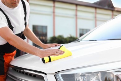 Photo of Man wiping car hood with yellow microfiber rag outdoors, closeup
