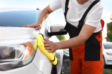 Photo of Man wiping car with yellow microfiber rag outdoors, closeup