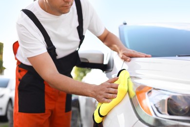 Photo of Man wiping car with yellow microfiber rag outdoors, closeup