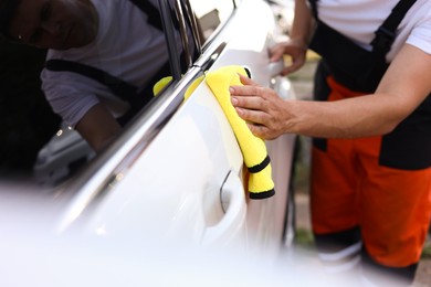 Photo of Man wiping car with yellow microfiber rag outdoors, closeup