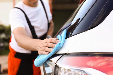 Photo of Man wiping car with blue microfiber rag outdoors, closeup
