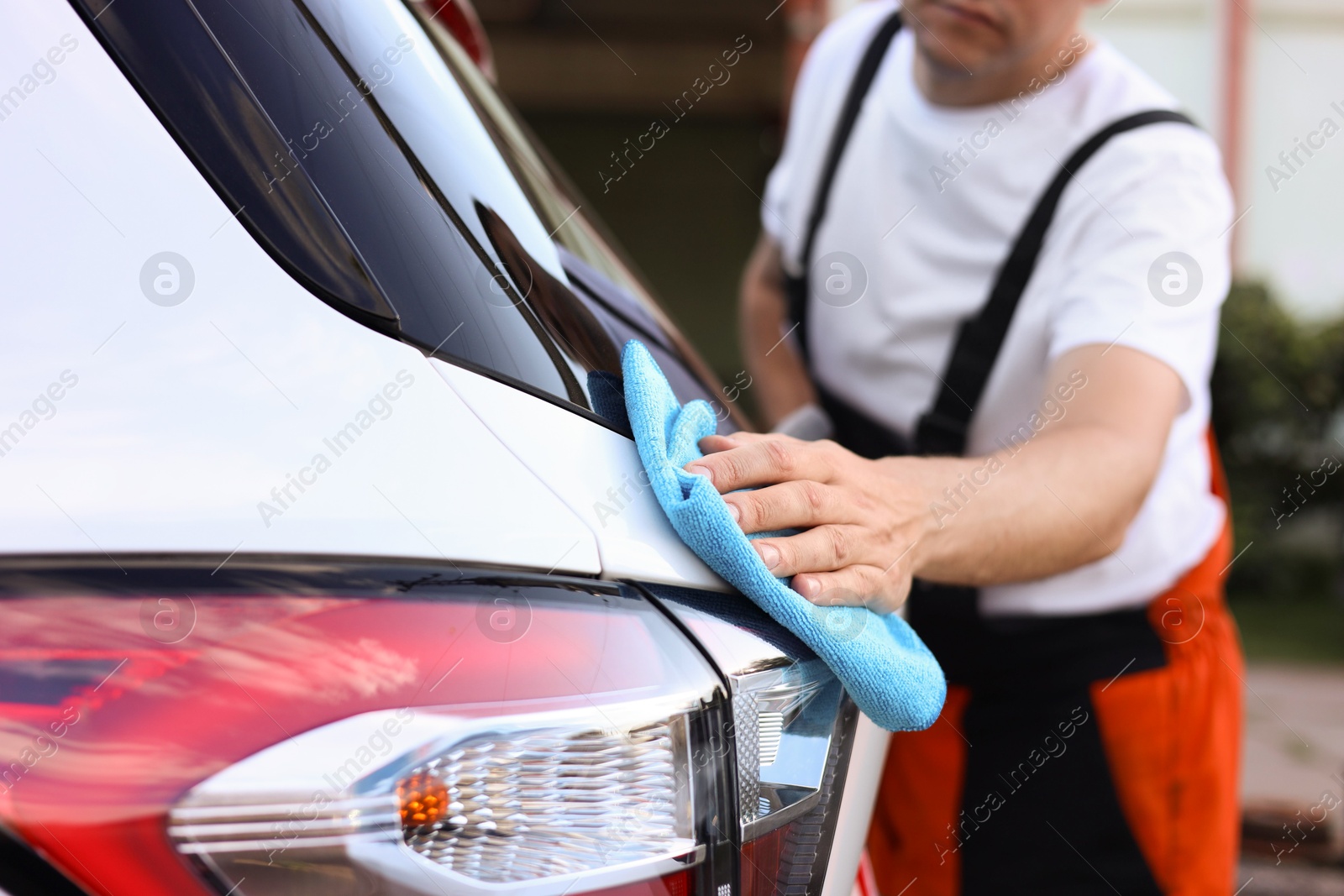 Photo of Man wiping car with blue microfiber rag outdoors, closeup