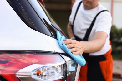 Photo of Man wiping car with blue microfiber rag outdoors, closeup