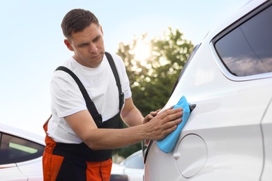 Photo of Man wiping car with blue microfiber rag outdoors