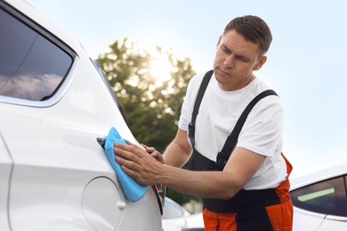 Photo of Man wiping car with blue microfiber rag outdoors