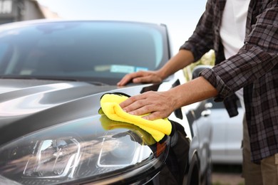 Photo of Man wiping car with yellow microfiber rag outdoors, closeup