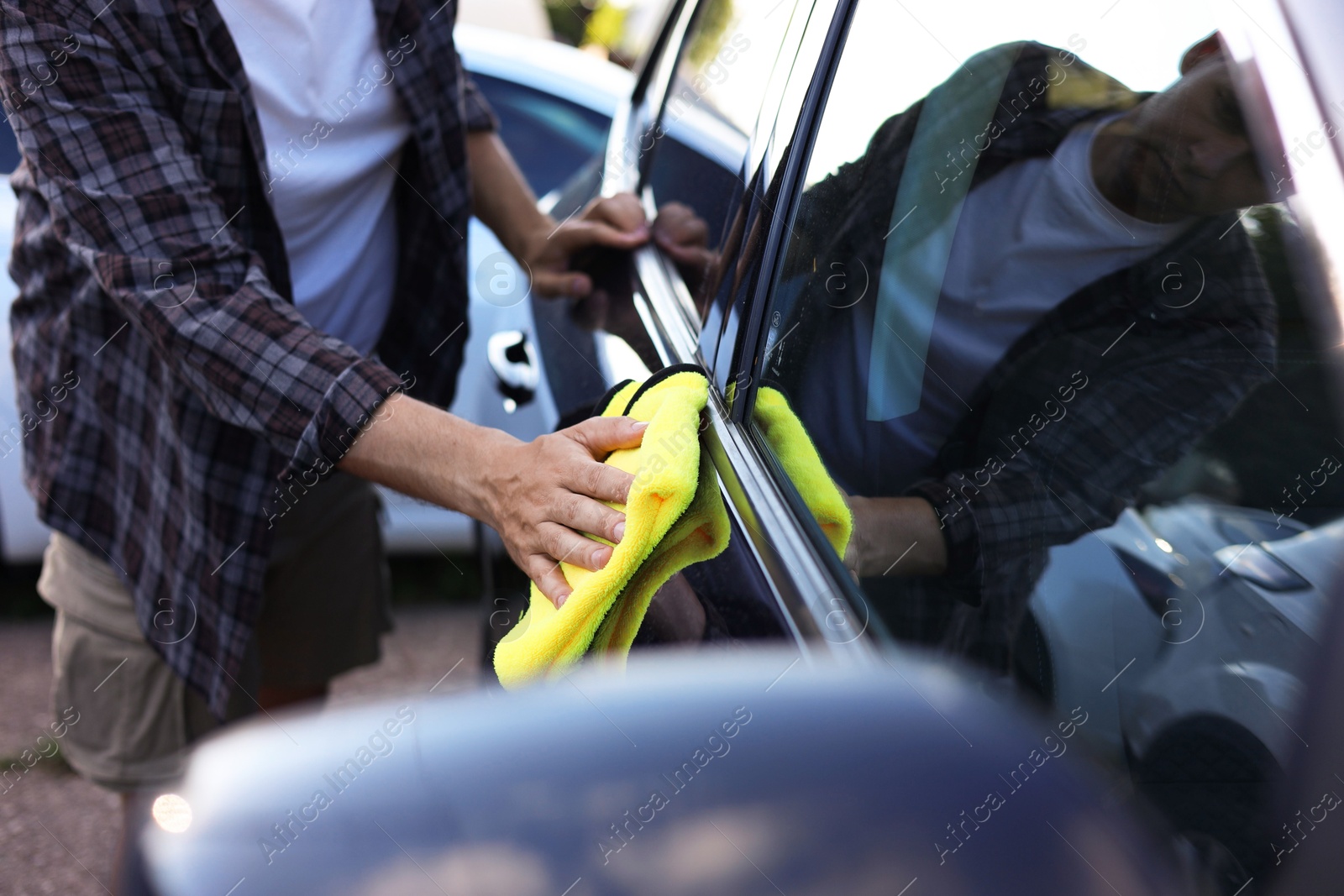Photo of Man wiping car with yellow microfiber rag outdoors, closeup